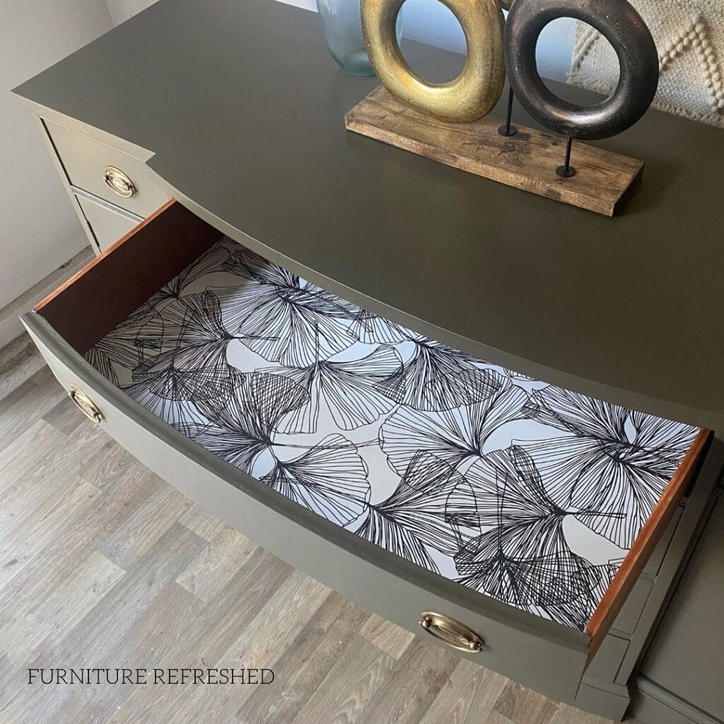Vintage gray console table with artistic drawer liner featuring black line art leaf pattern.