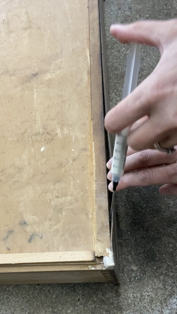Using a blunt end syringe filled with wood glue to repair veneer.