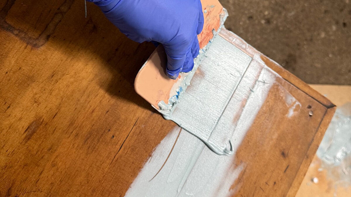 Spreading Bondo over a piece of wood furniture.