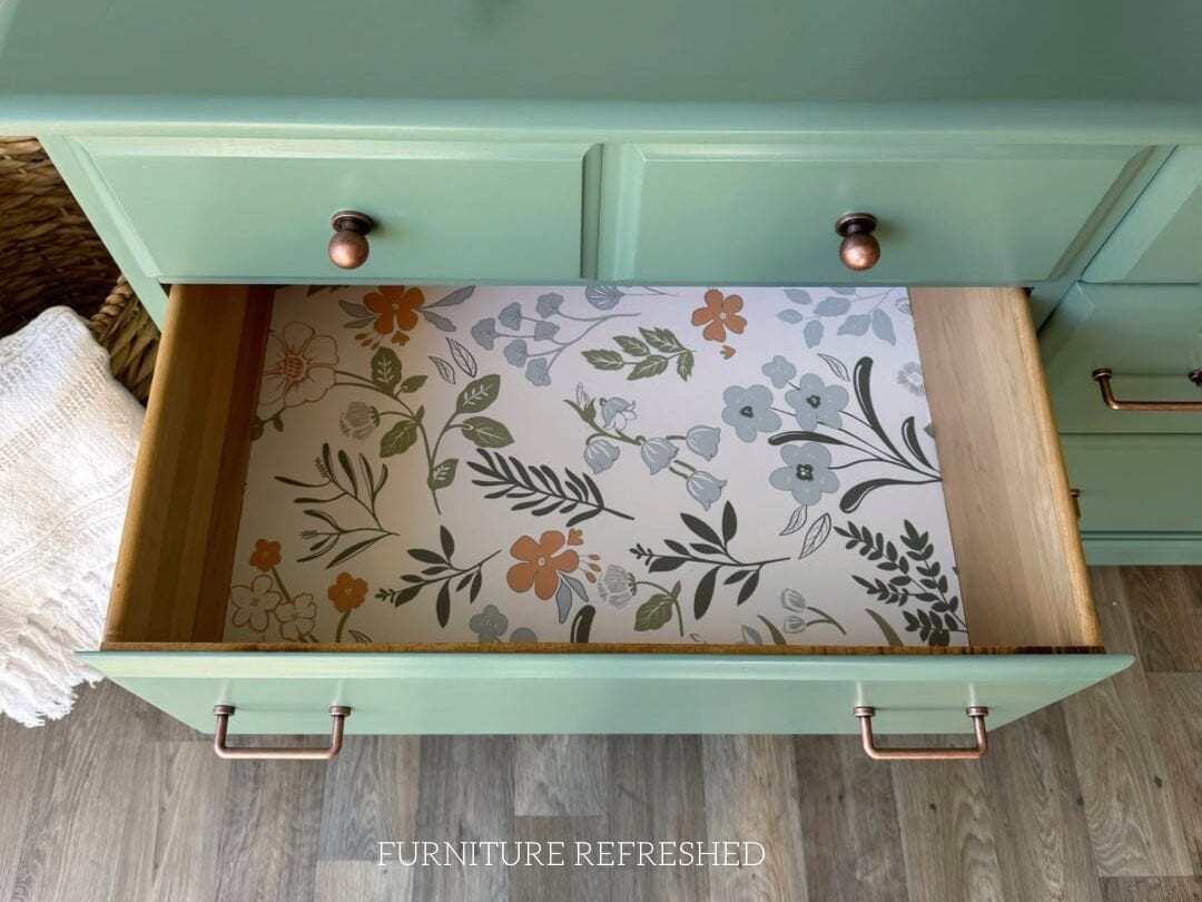 Closeup photo of green dresser with a drawer open, highlighting a floral wallpaper drawer liner inside.