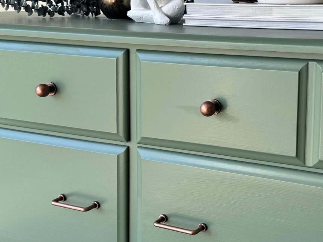 Close up photo of dresser drawers with green paint and antique copper hardware.