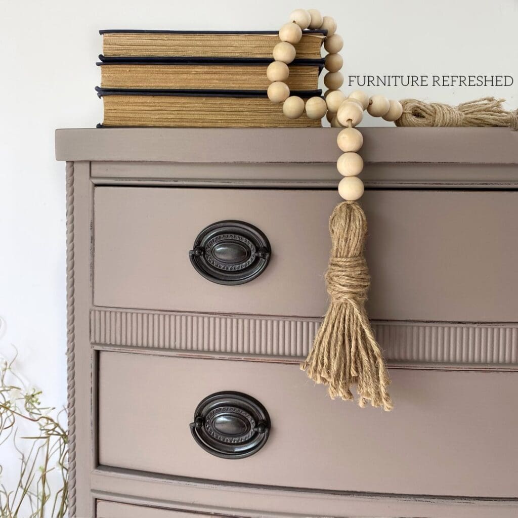 Close up of the corner of a beige dresser drawer with Hepplewhite style hardware.