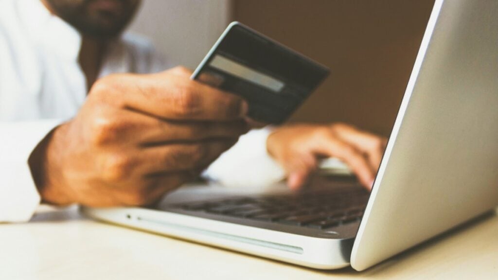 Person holding a credit card in front of a computer.
