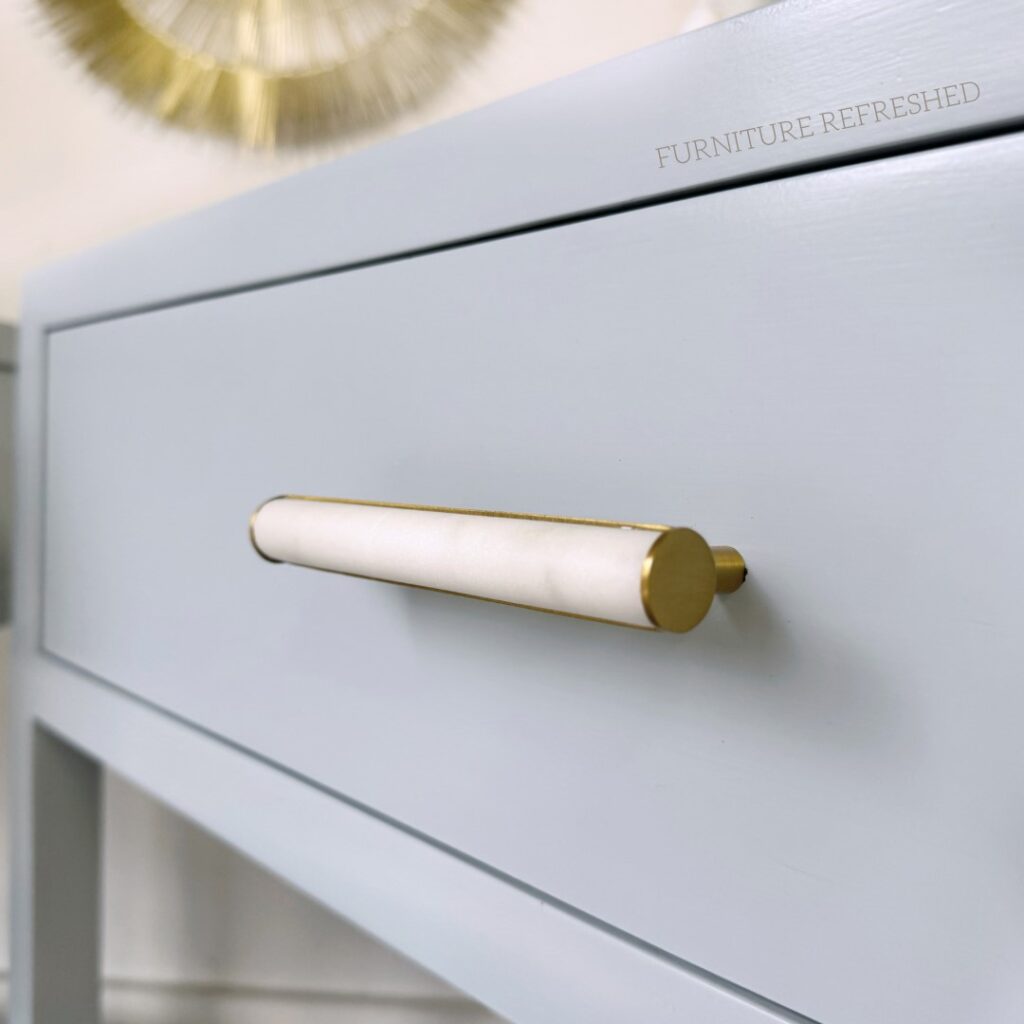 Close of up drawer hardware on a bedside table. Hardware is marble and brass, table is a light blue color.