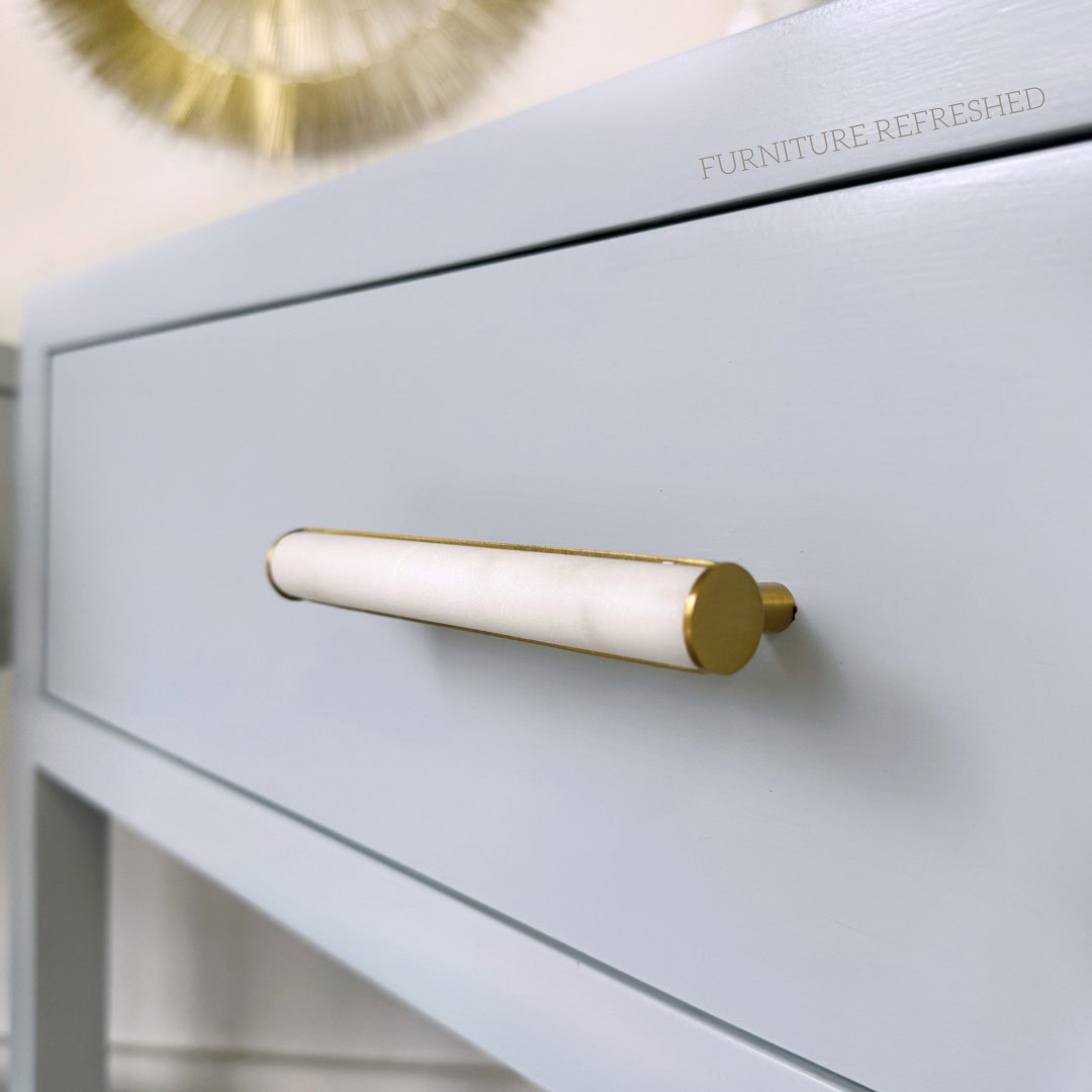 Close of up drawer hardware on a bedside table. Hardware is marble and brass, table is a light blue color.