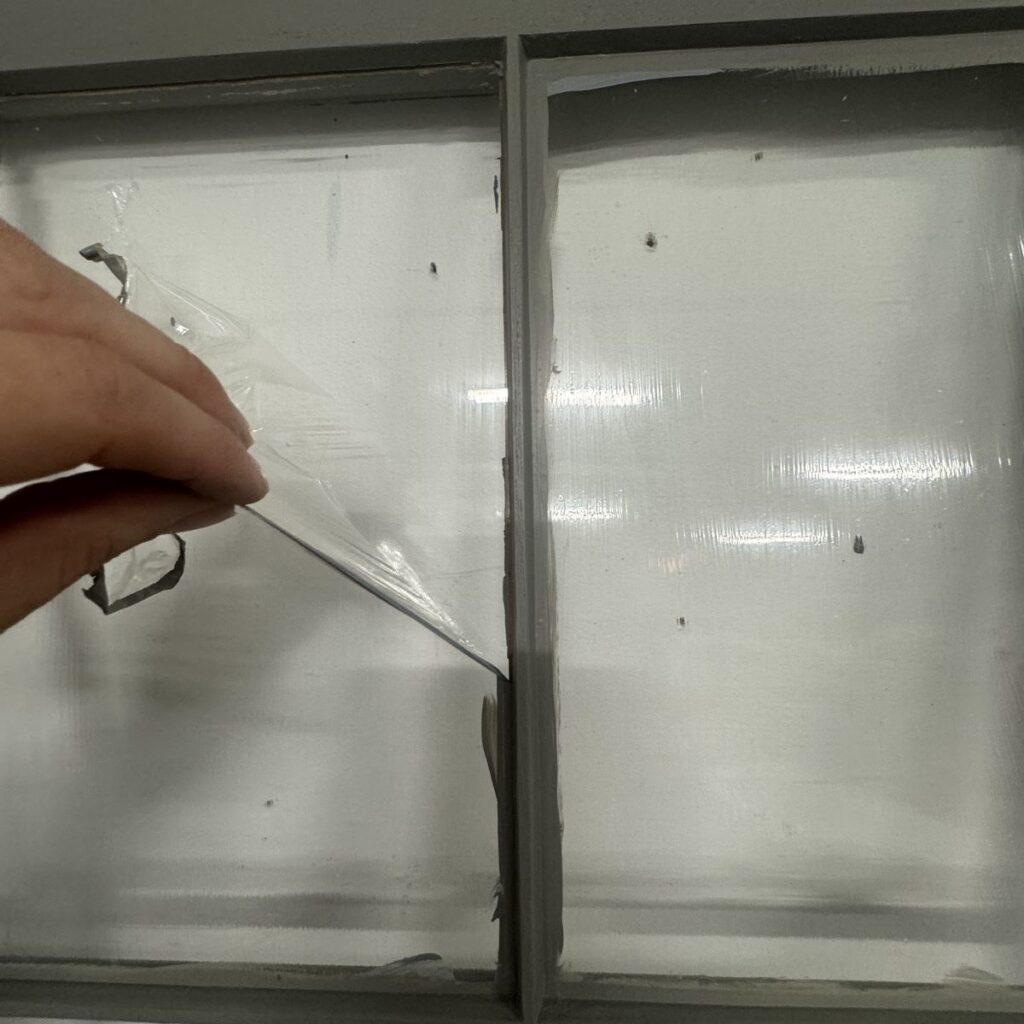 Photo of a person peeling off the liquid mask from a window pane.