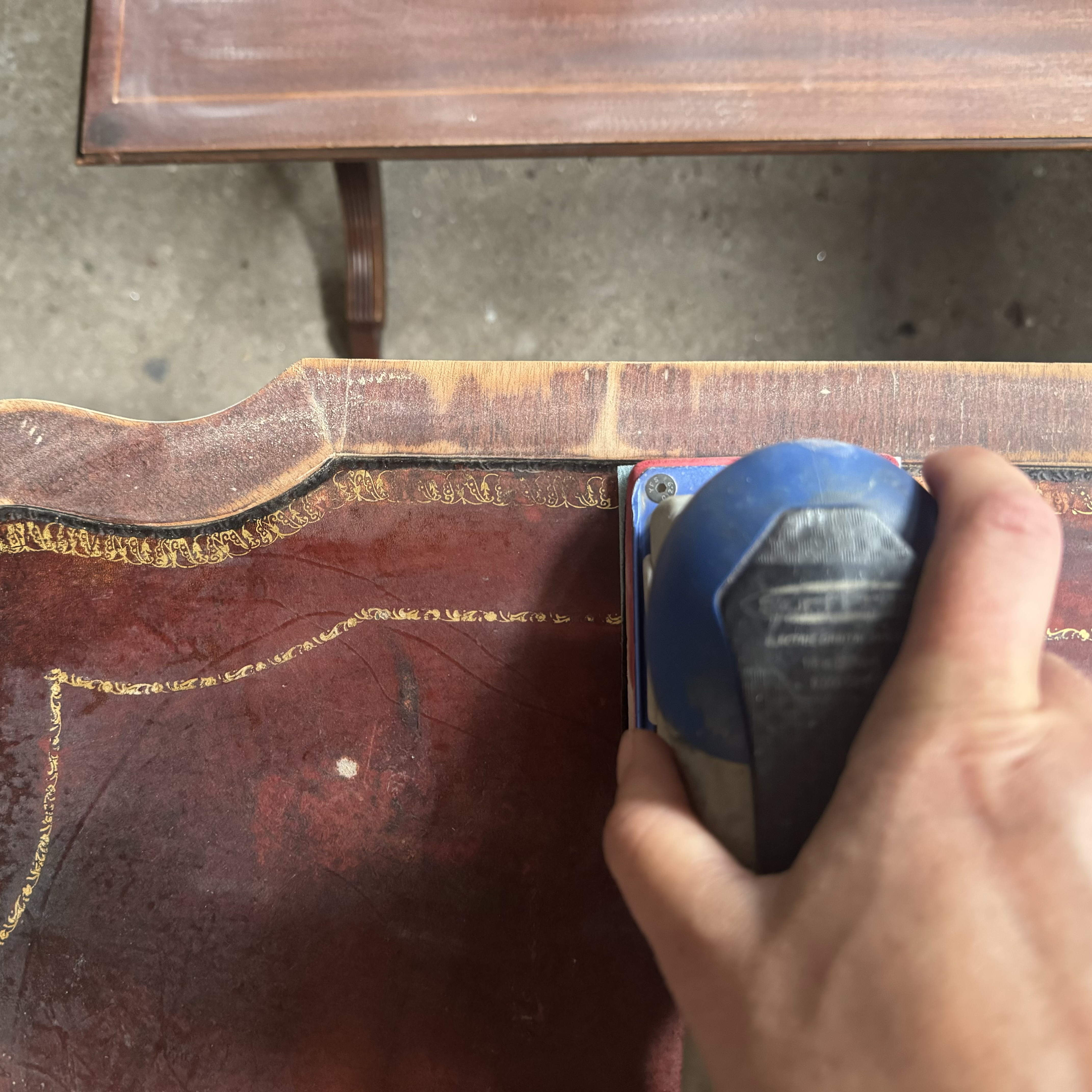 A close-up photo of me sanding the leather top using an electric sander.