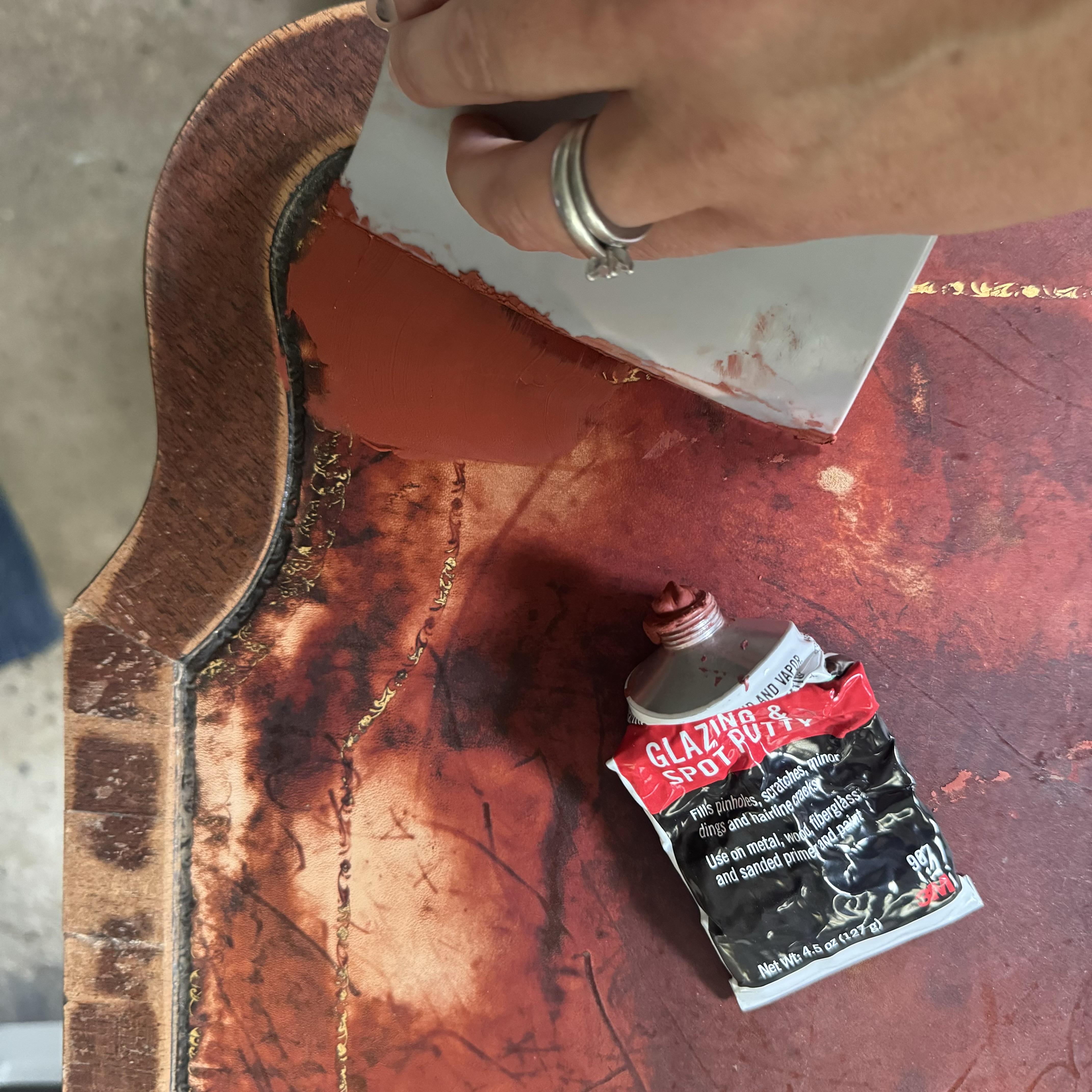A close up photo of me spreading Bondo glazing and spot putty to smooth out the leather surface on the table.