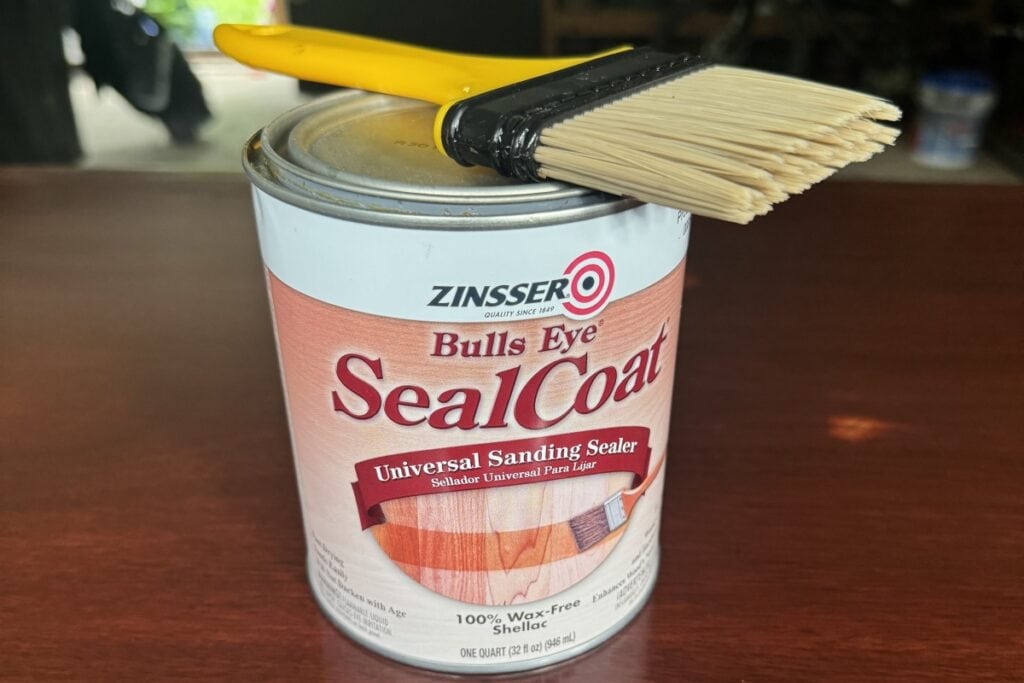 Photo of Zinsser Seal Coat, the clear shellac product I used to prime this sideboard. A plastic yellow chip brush is lying on top of the can of shellac.