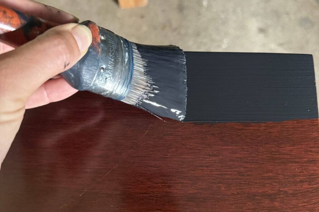 A clloseup photo of a paintbrush laying black paint on the top of the sideboard.