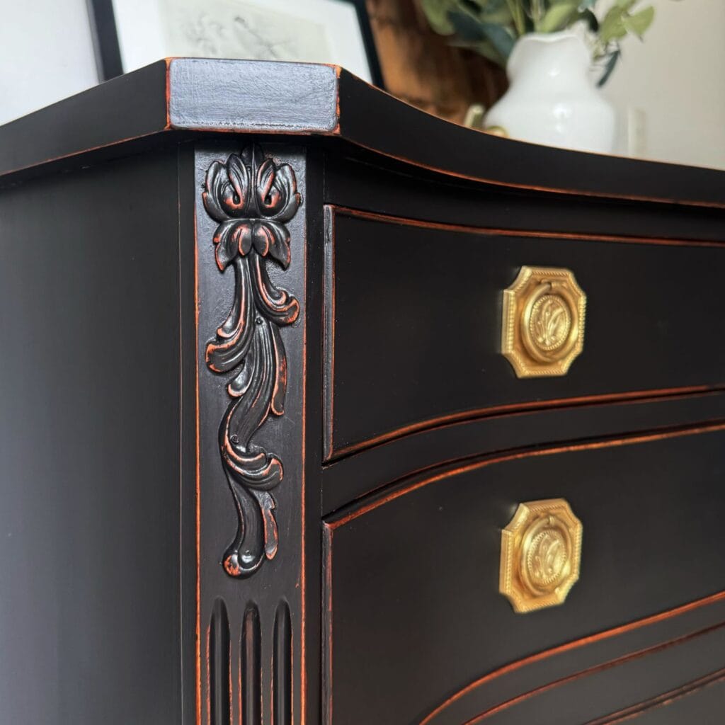 Close up photo of the painted and distressed sideboard. Side angled view of the top conner with the top two drawers partially visible and you can see the wood on the edges of the drawers and the detailed woodwork on the sides.