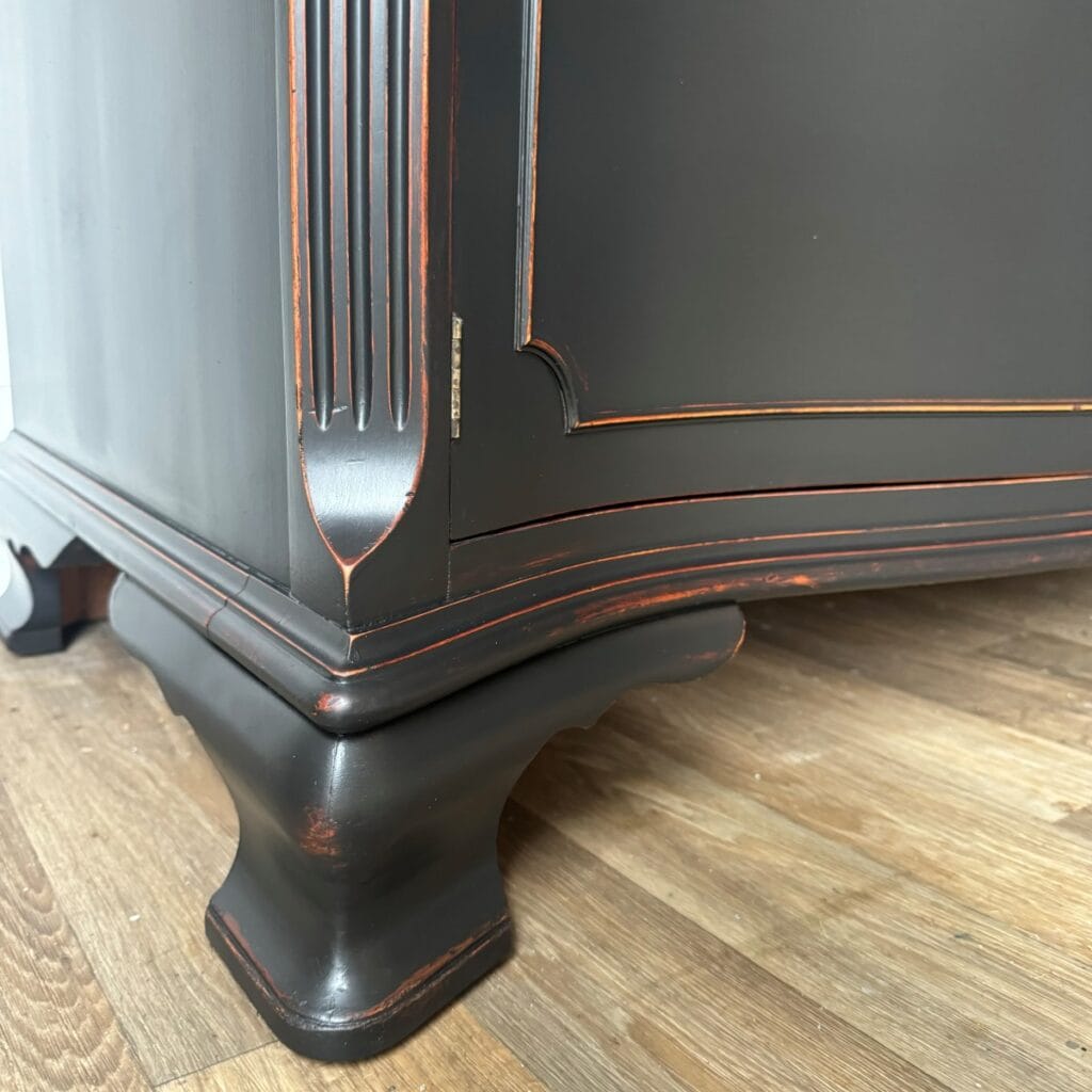 Close up of the base of the sideboard that has been painted black and distressed. You can see the wood peeking through the details on the legs.