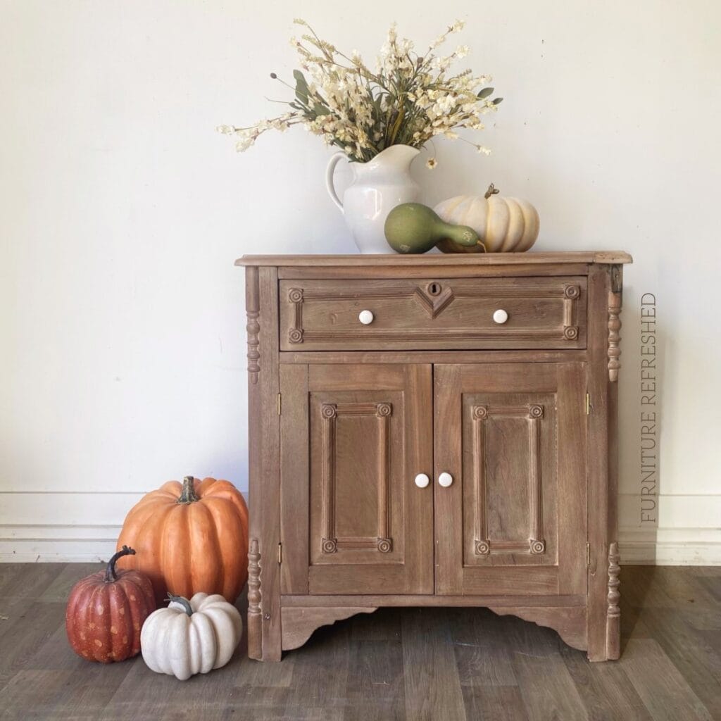 Antique walnut washstand that has been stripped and refinished with a raw wood look. Ceramic white knobs complete the look. Pumpkins and gords are placed on top and on the side as decor.