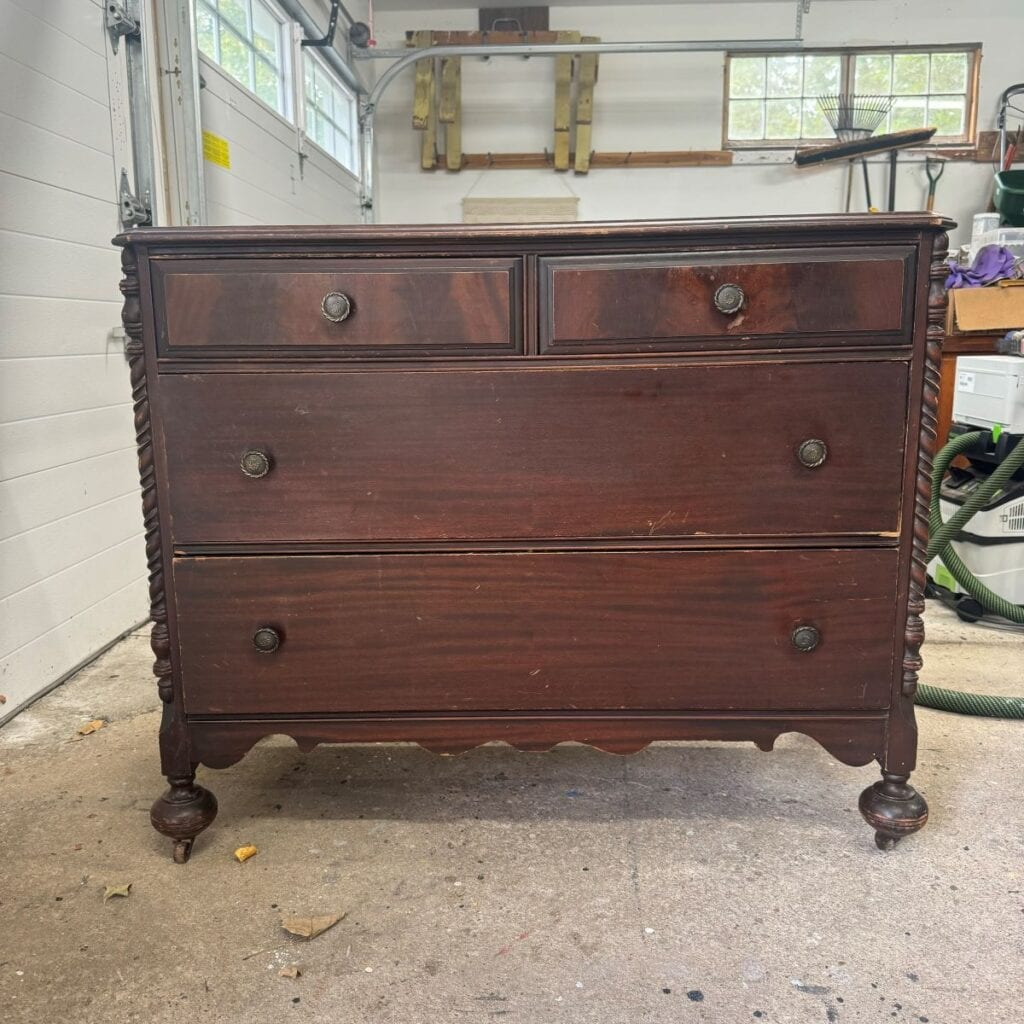 Before photo of the dresser used in the makeover. It has 4 drawers and bun feet. It is stained dark brown.