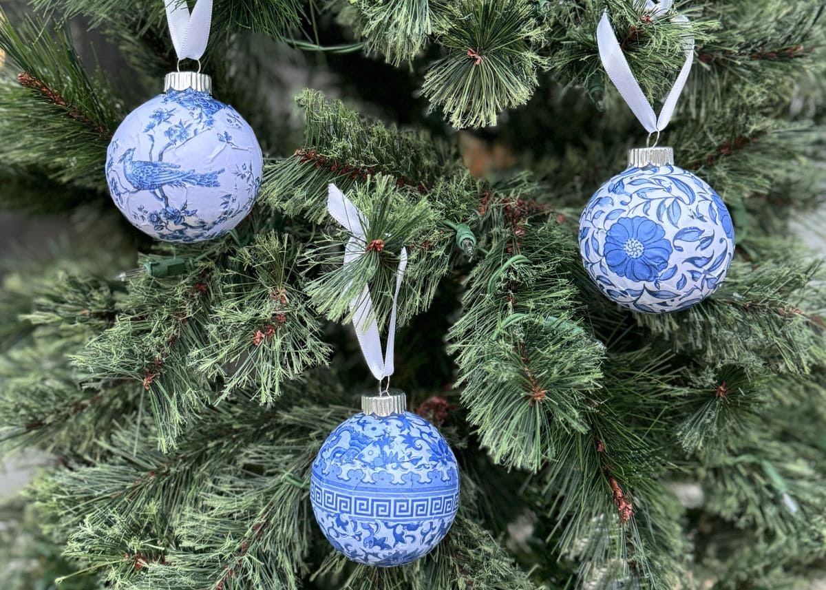 Photo of 3 Chinioserie style round Christmas ormaments with white ribbons hanging on a tree.