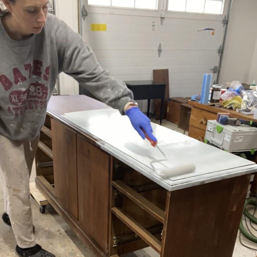 Photo of person woman rolling primer onto the top of a large credenza.