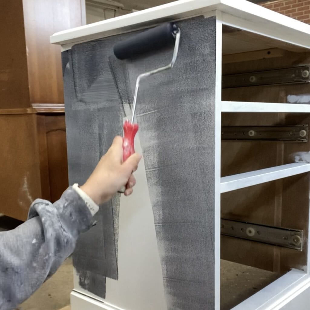 Using a roller to apply the navy paint glaze to the side of the dresser.
