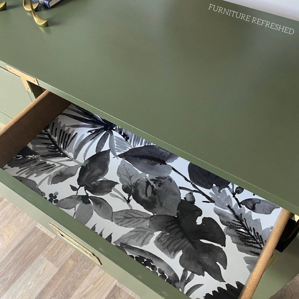 Close up of lined drawer with black tropical leaves peel and stick wallpaper.