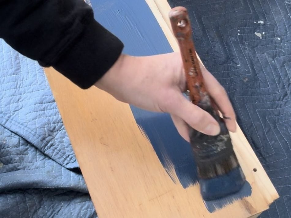 Photo of a person hand painting furniture (a drawer) with a brush.