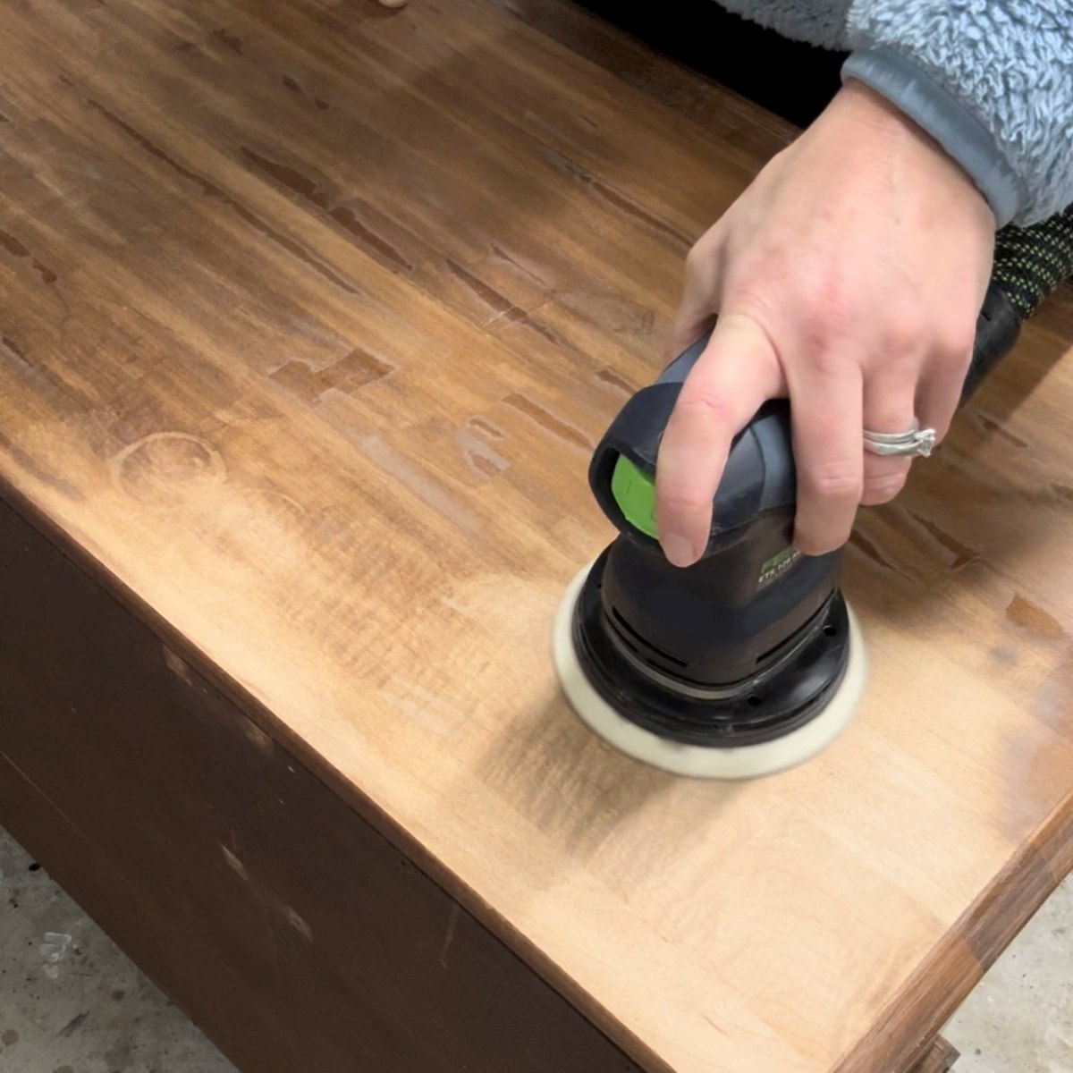 Using an orbital sander to sand the finish off of a dresser top.