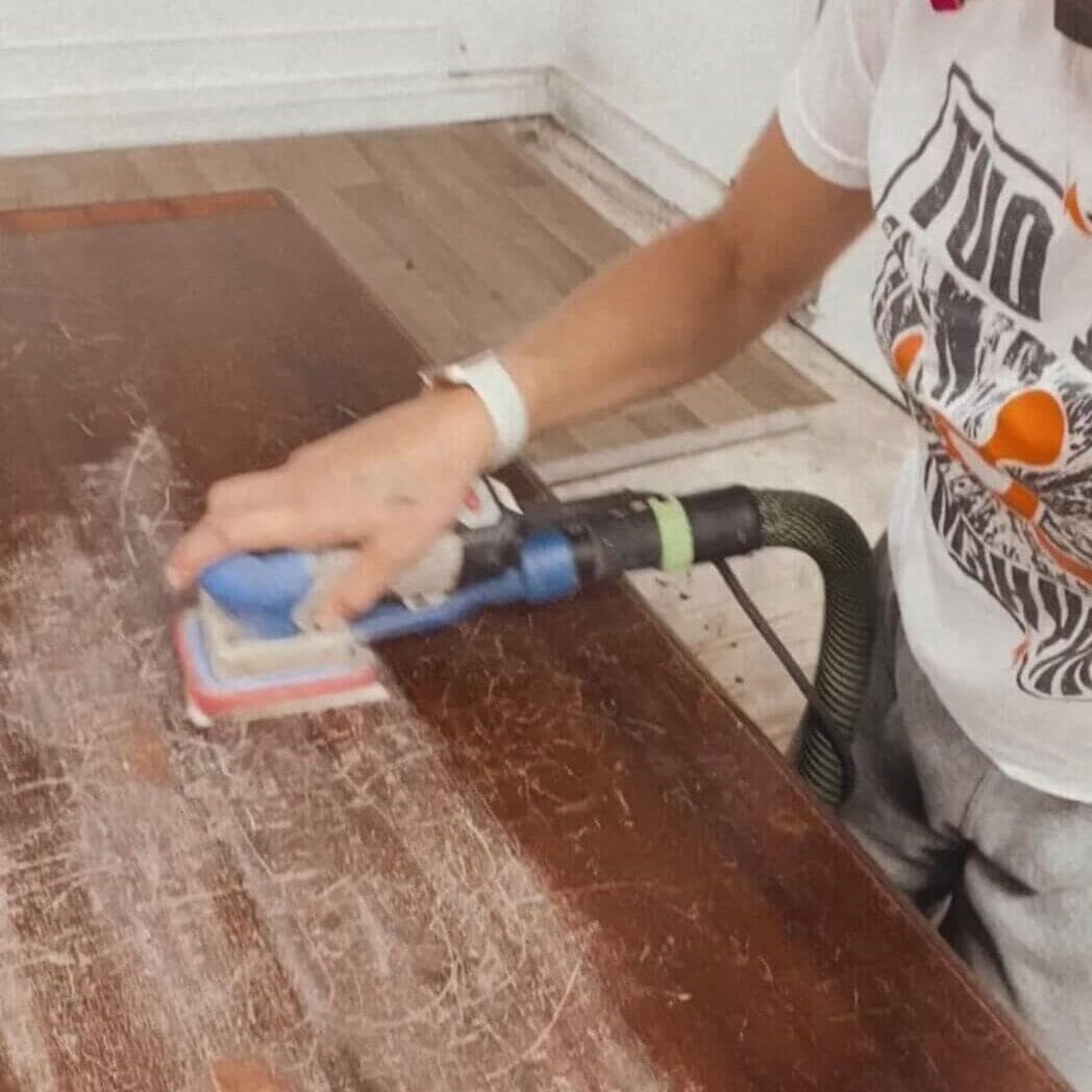 Preparing a piece of furniture for paint by scuff sanding with an electric sander.