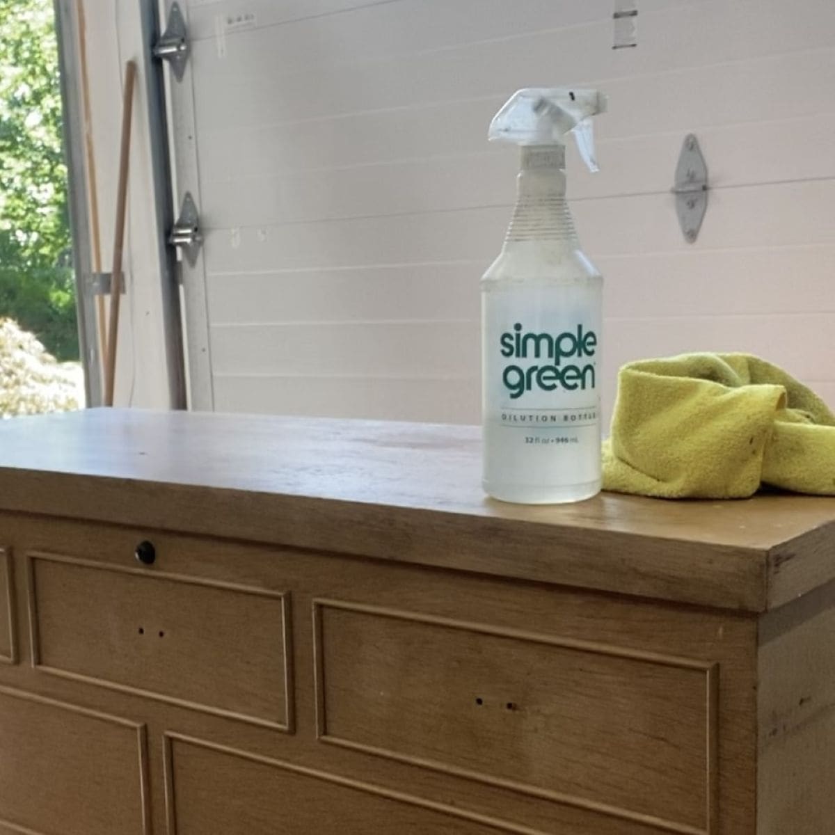 A photo of Simple Green Cleaner and a microfiber cloth on to of a piece of vintage furniture.