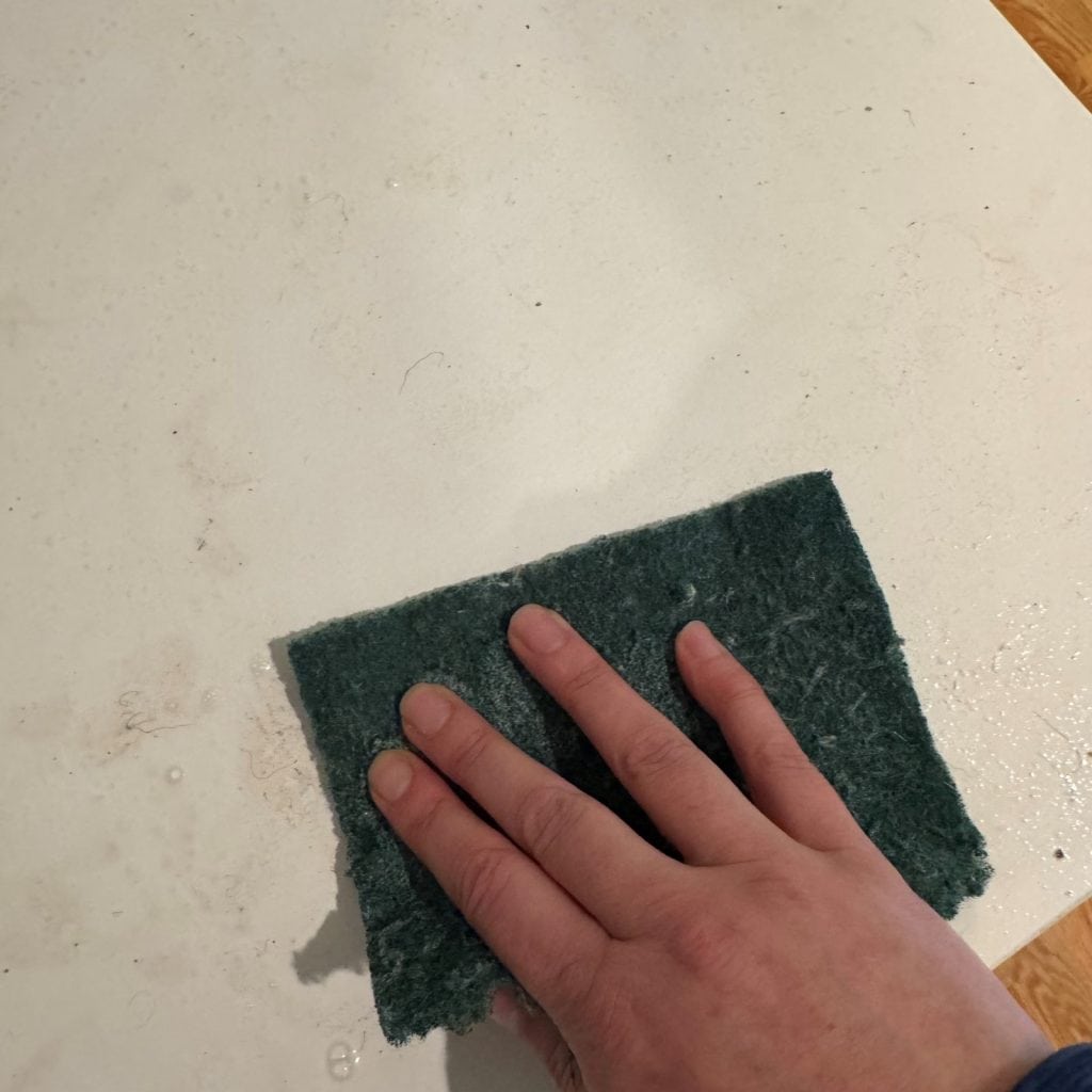 Close up of cleaning the countertop with a green scotchbrite pad.