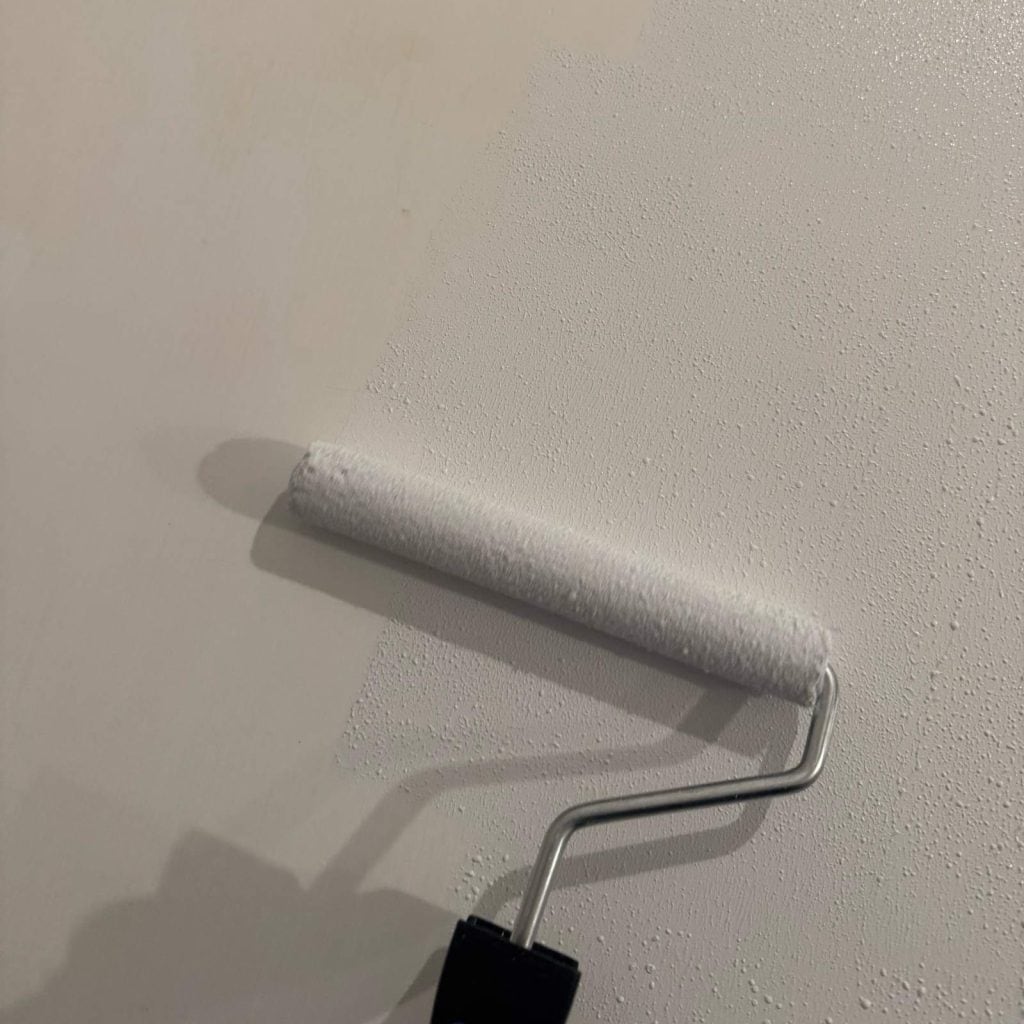 Using a paint roller to roll white primer onto the countertop