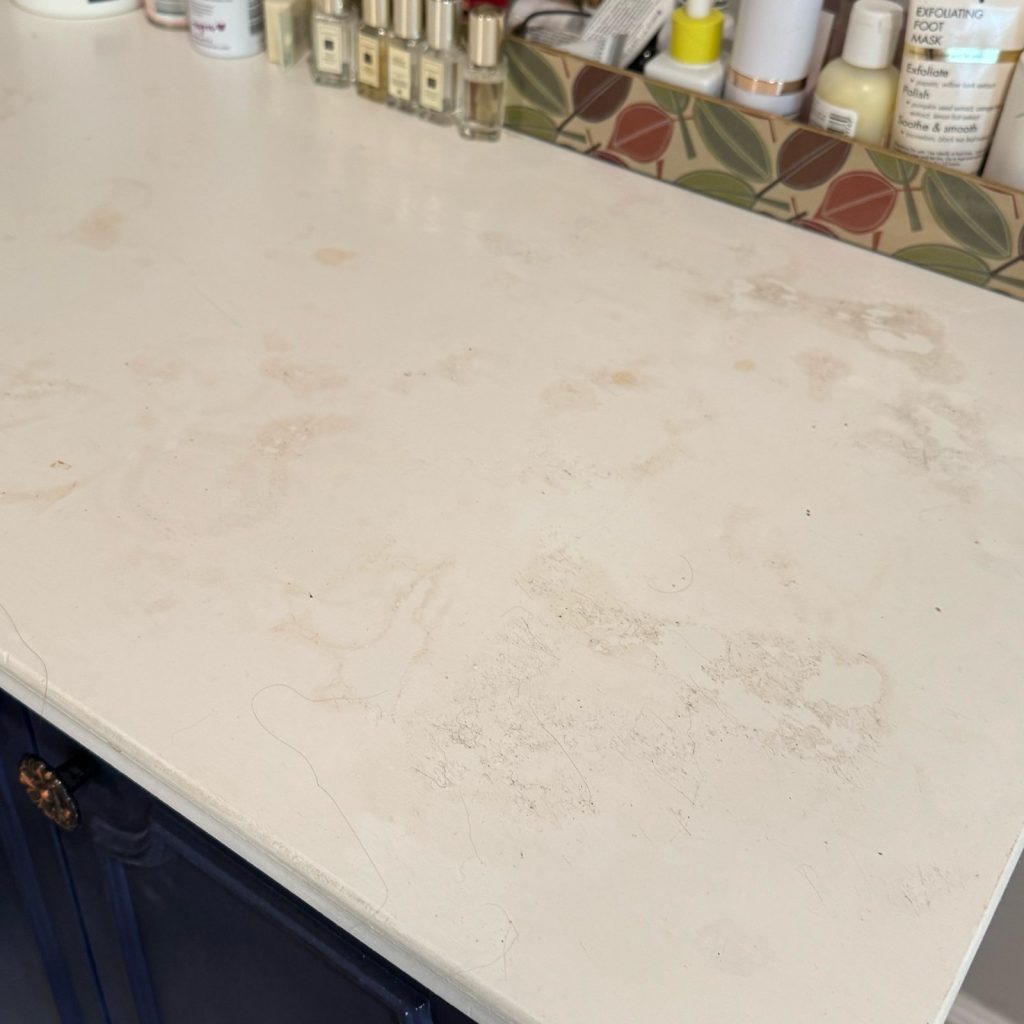 Closeup before photo of painted white vanity countertop that has been wrecked by using hair and makeup products.