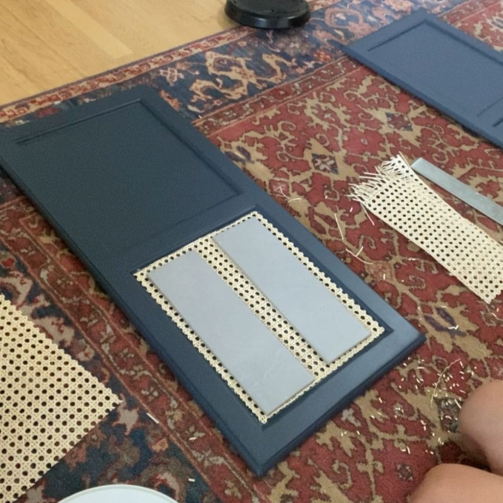 A door panel with cane webbing glued onto the front. Gray tiles are being used to hold the cane down while the glue dries.