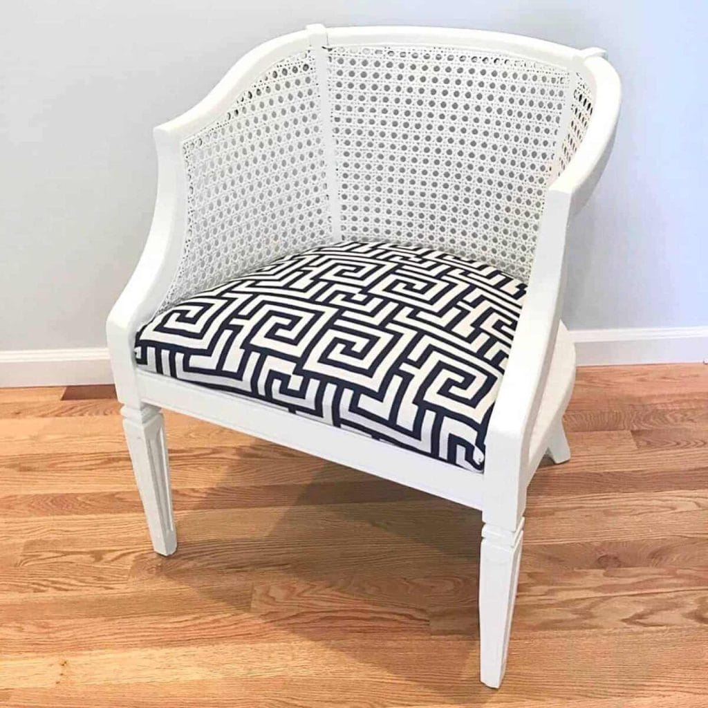 After photo of caned club chair painted white with a blue and white geometric patterned fabric seat.