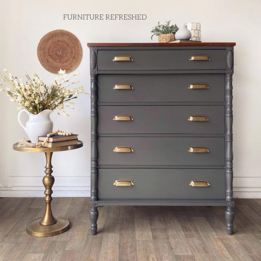 A gray dresser with brass hardware and a vase on the side.