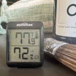 photo of a digital thermometer with temperature and humidity displayed, sitting next to paint and a paintbrush.