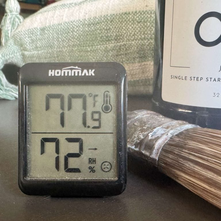 photo of a digital thermometer with temperature and humidity displayed, sitting next to paint and a paintbrush.