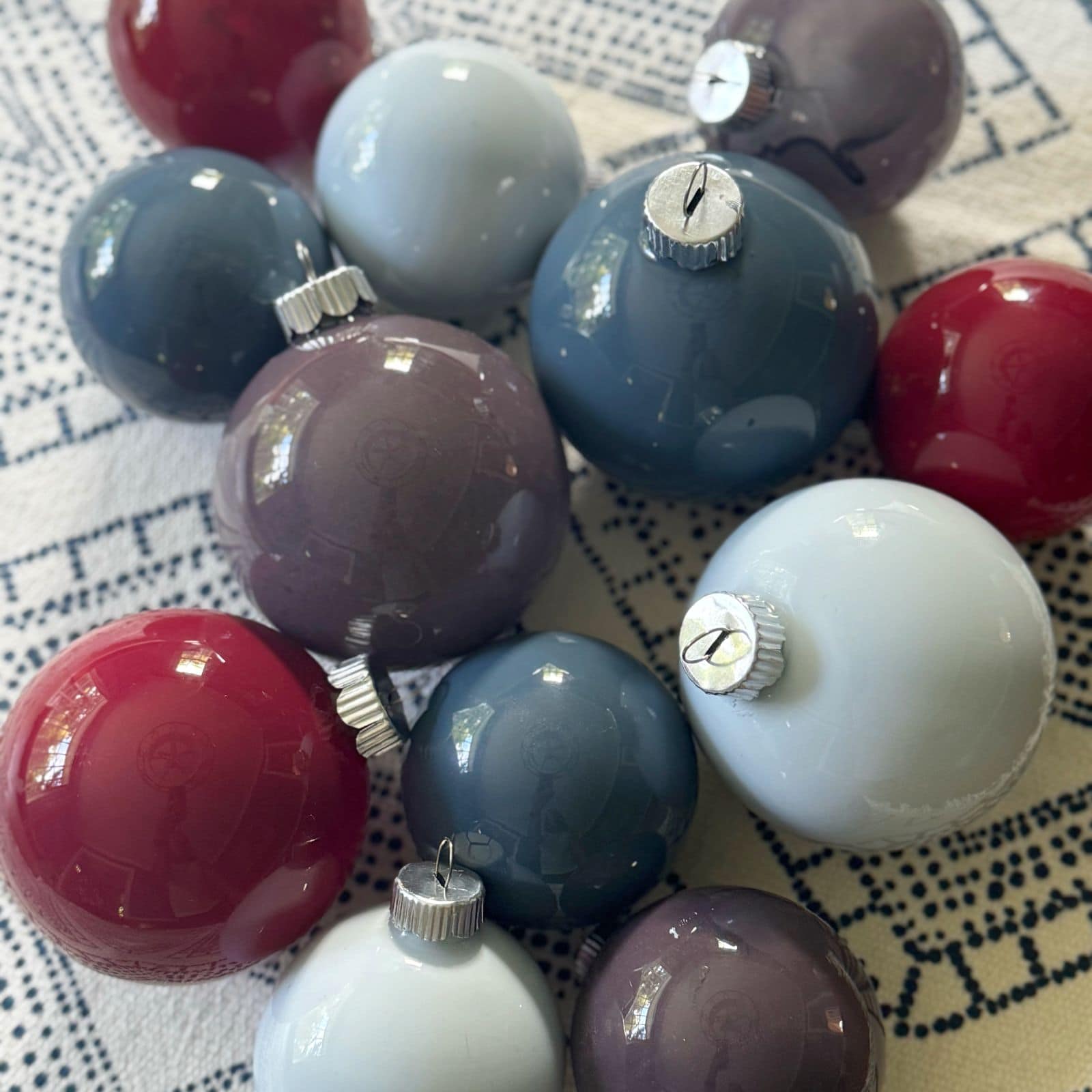 DIY colored Christmas ornaments laid out on a tablecloth backdrop.