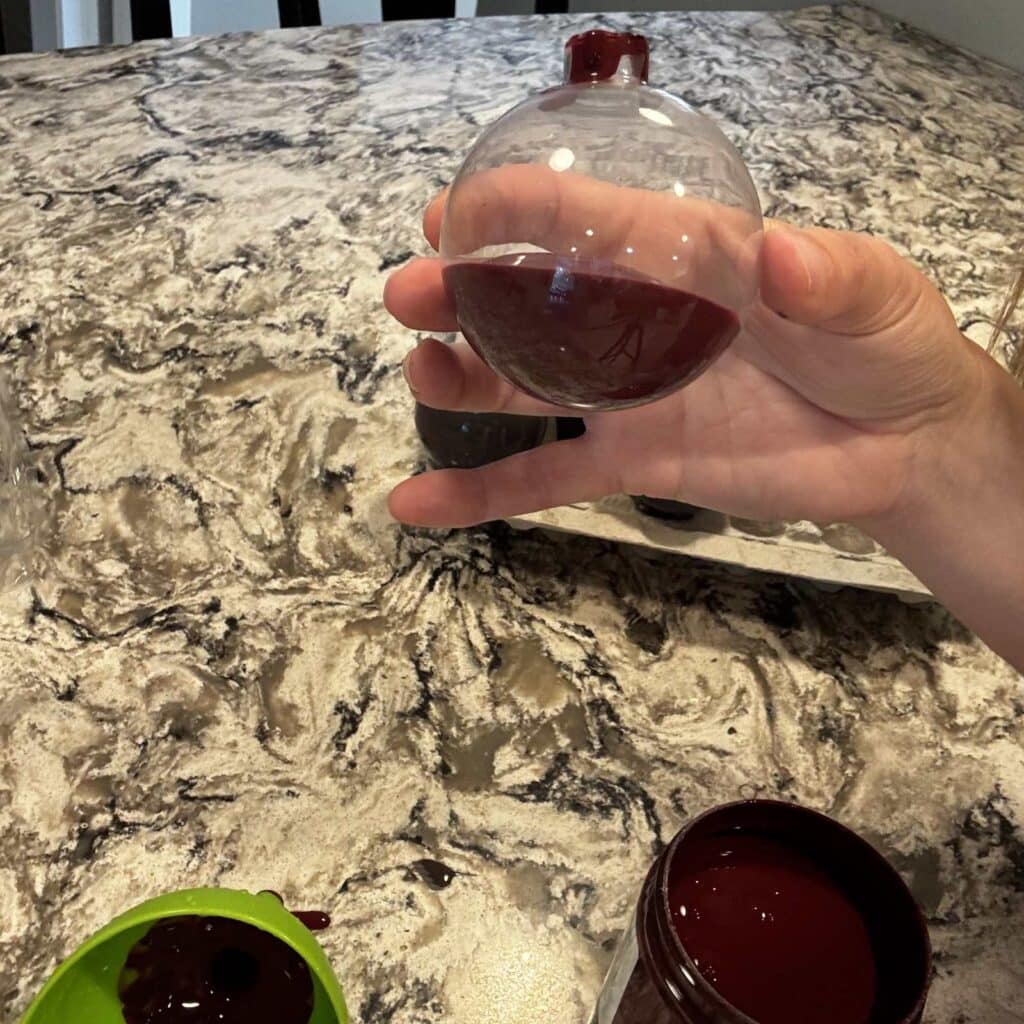An glass ornament with filled about a quarter full with red paint.