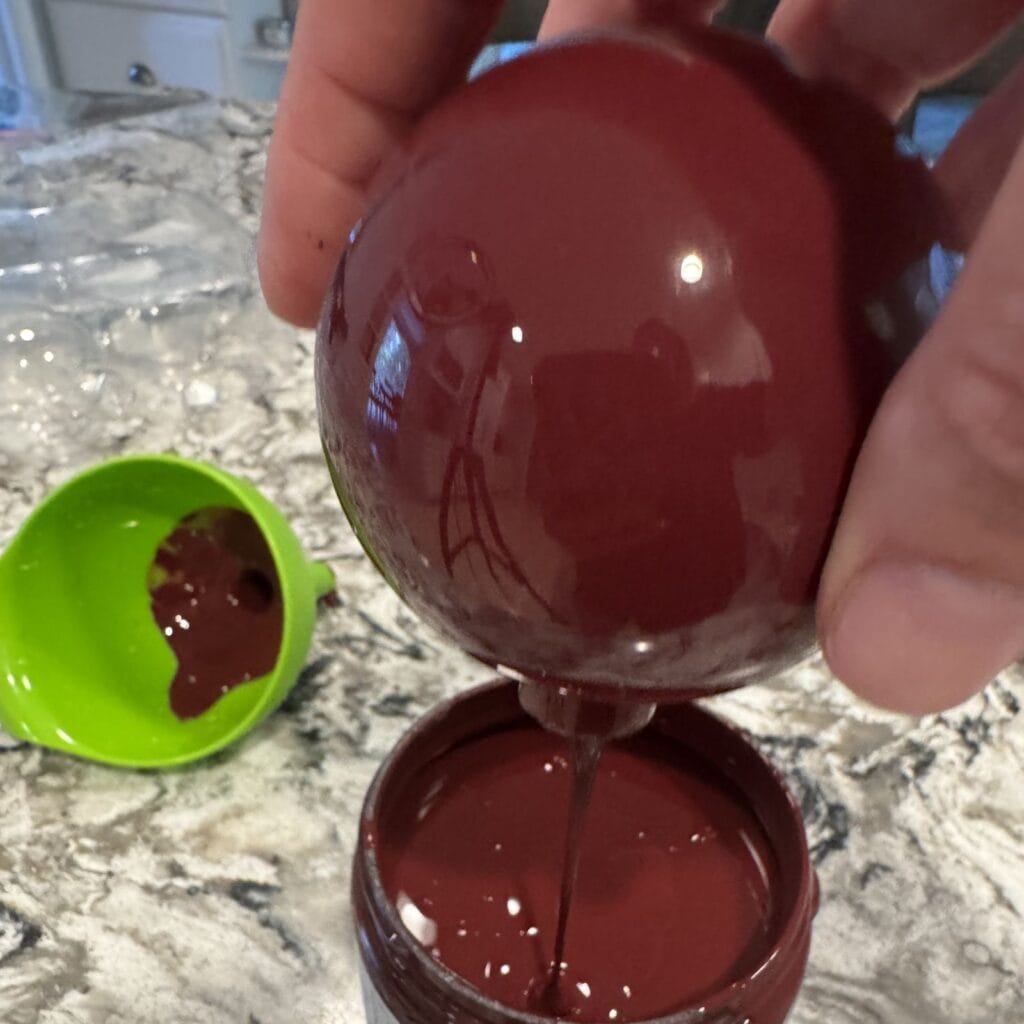 A glass ornament turned upside down to pour out excess paint back into paint jar.