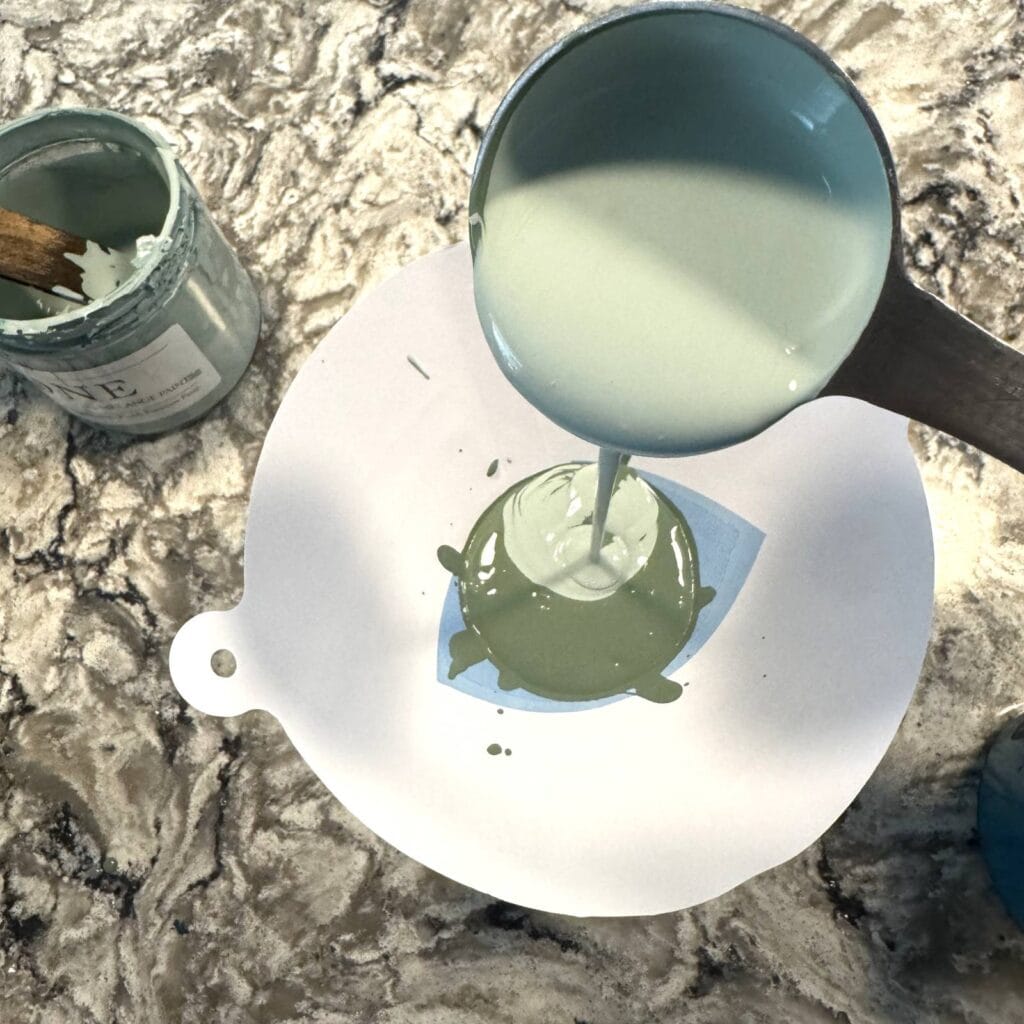 Pouring a light green paint into a strainer with a darker green paint already in it.