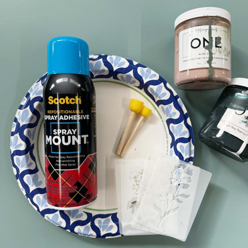 Photo of supplies for stenciling furniture: adhesive spray, stencils, stippling brushes, paint, paper plate.