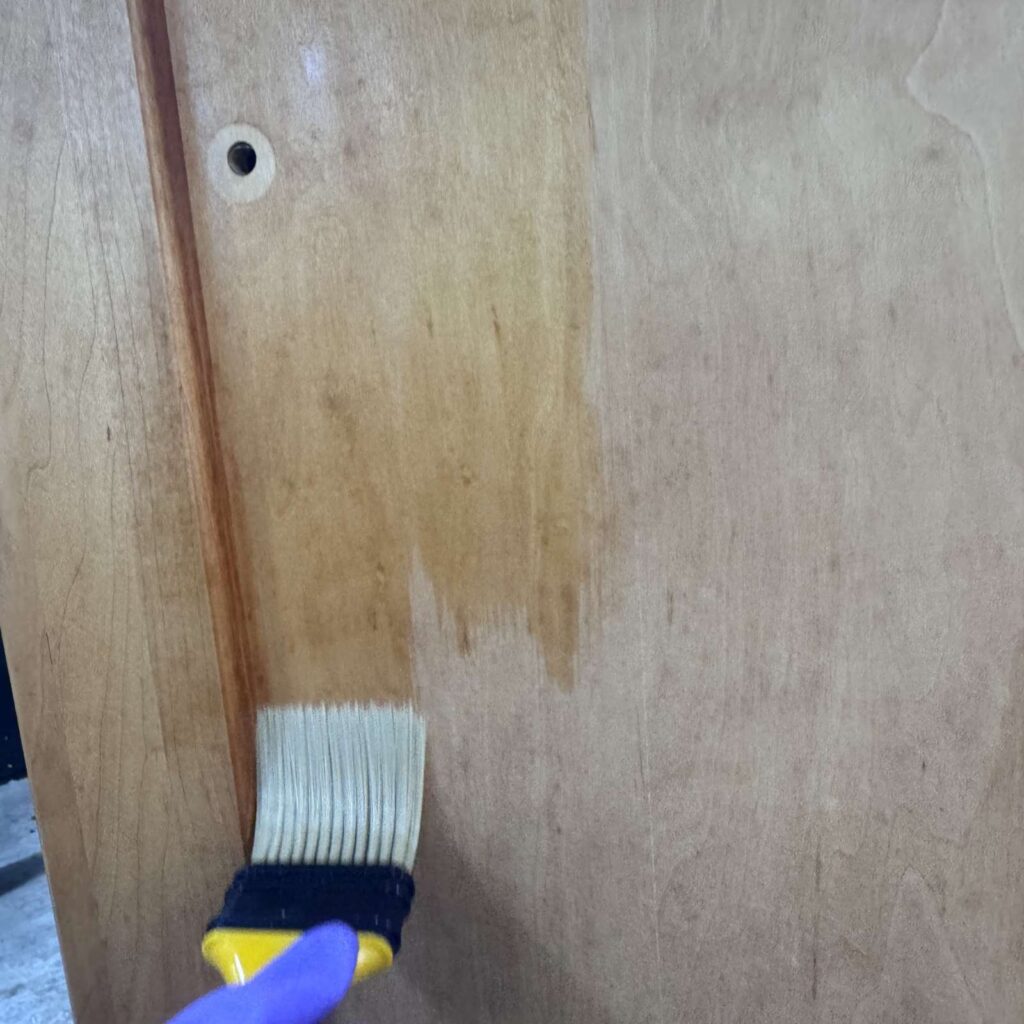 Applying bleach to the side of the cabinet with a chip brush.