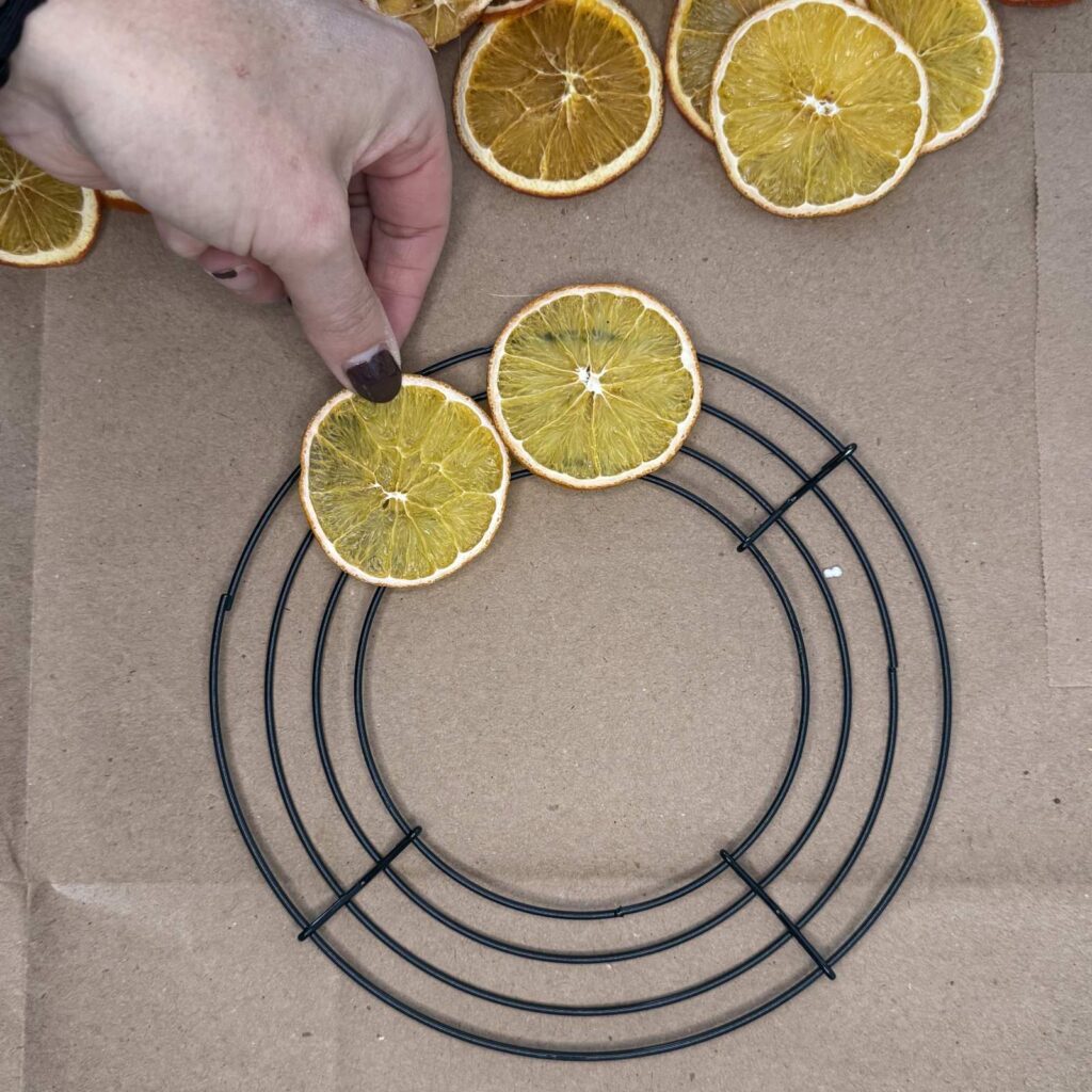 Gluing first orange slices to the metal wreath frame