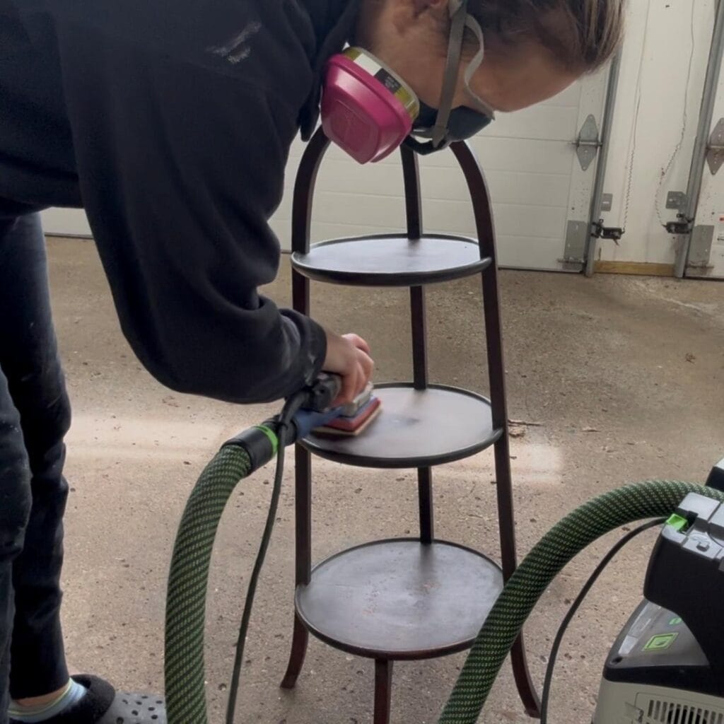 Lightly sanding the plant stand to prepare it for paint.
