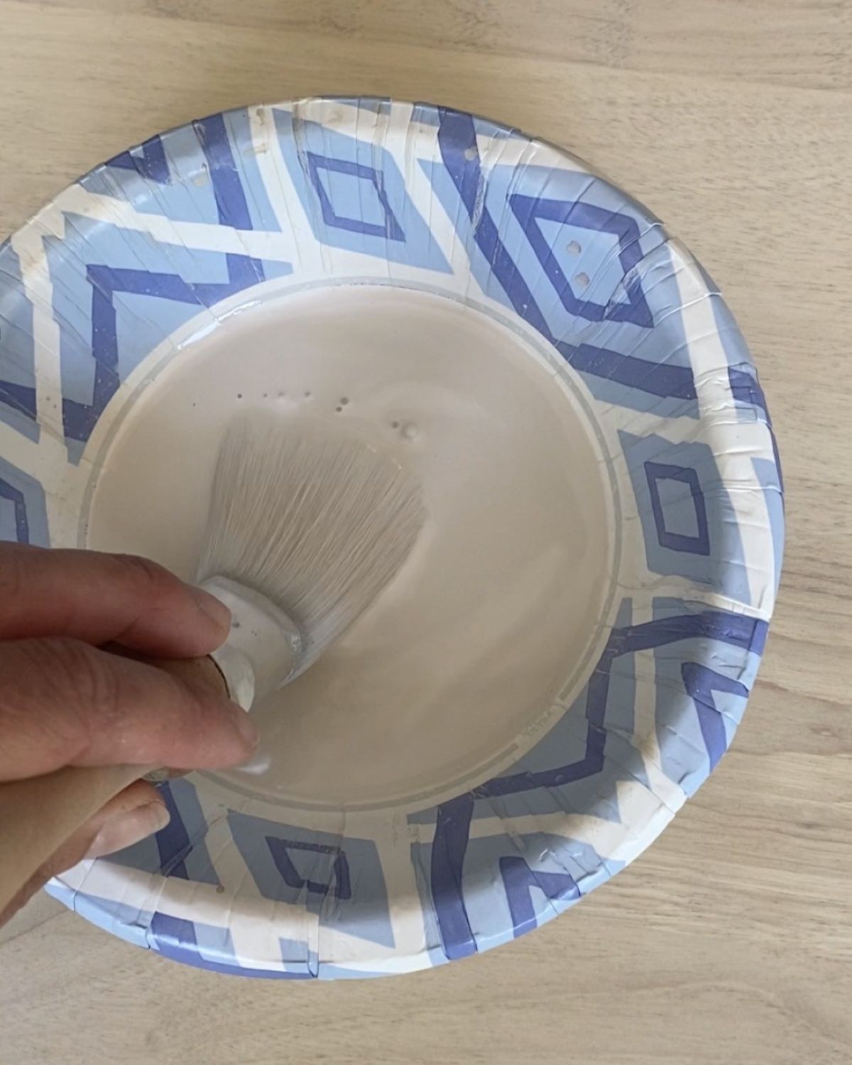 A bowl with water and paint mixed together to make a wash, being stirred by a paintbrush.